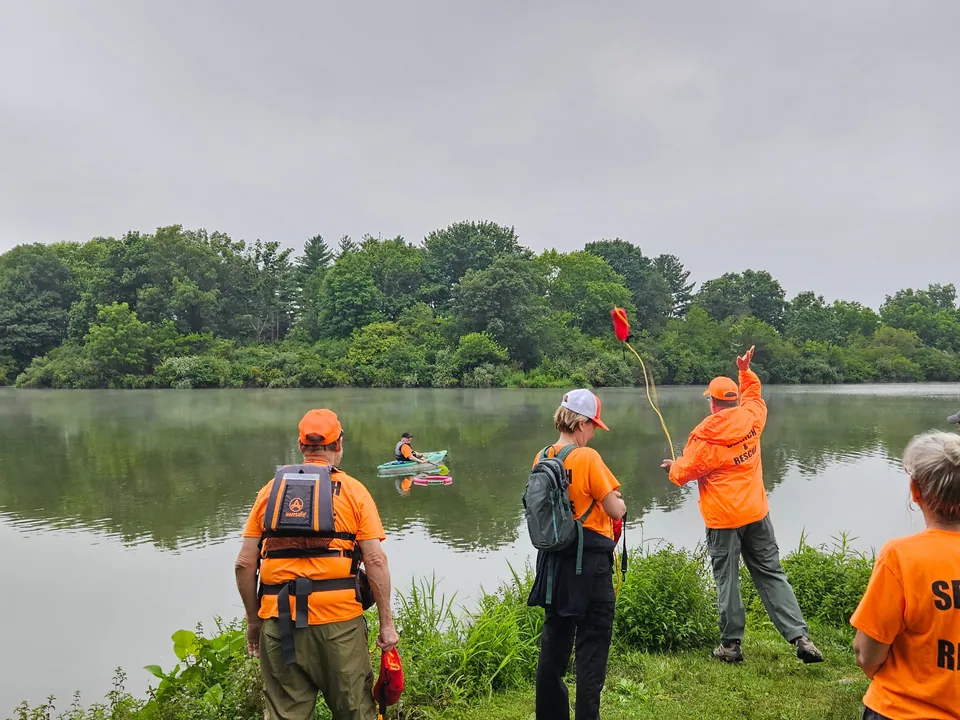 Searchers practice throwing a rescue line from the grassy shore of Homer Lake.